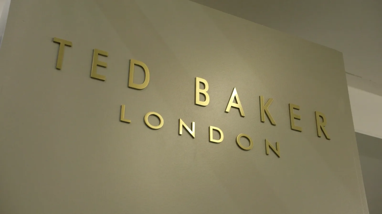 Brass Ted Baker London lettering on a cream wall.