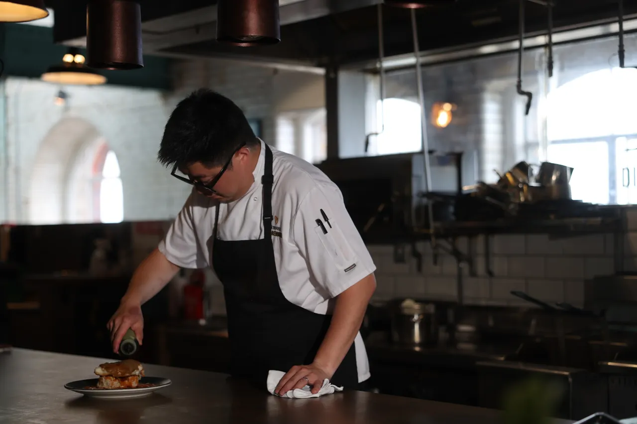 A chef in whites and a black apron finishes a plate on the pass in the 1837 Bar & Brasserie kitchen.