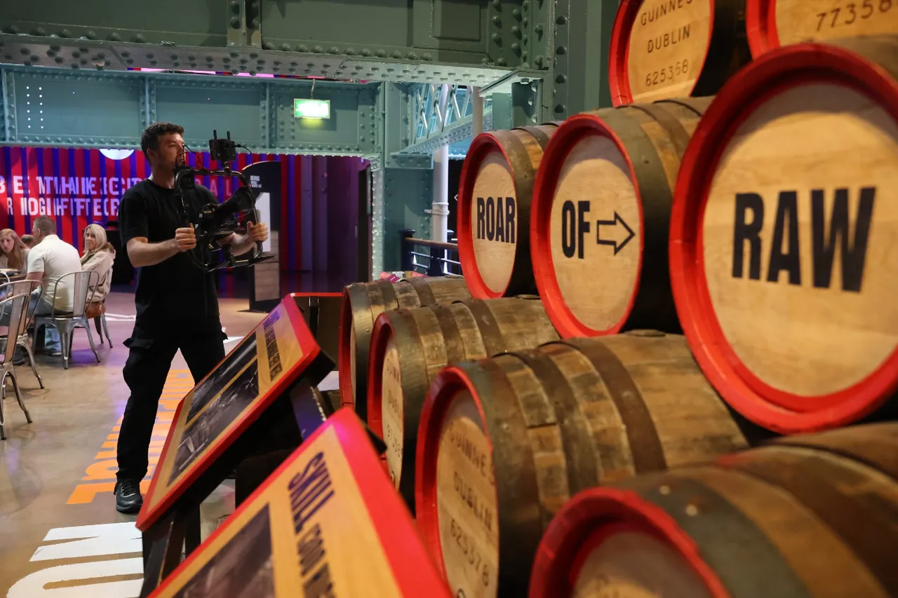 A camera operator with a stabilised rig films between stacked Guinness barrels painted with the words Roar of Raw.